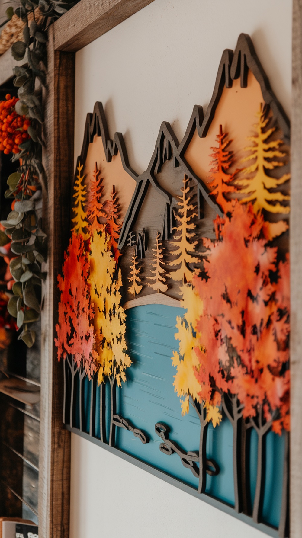 A layered wall art piece depicting colorful autumn trees, a blue lake, and mountains.