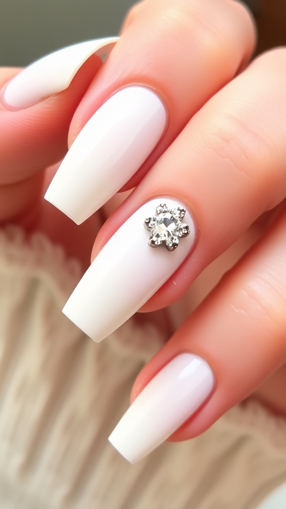 A hand with white French nails and one accent nail featuring rhinestones and floral design.