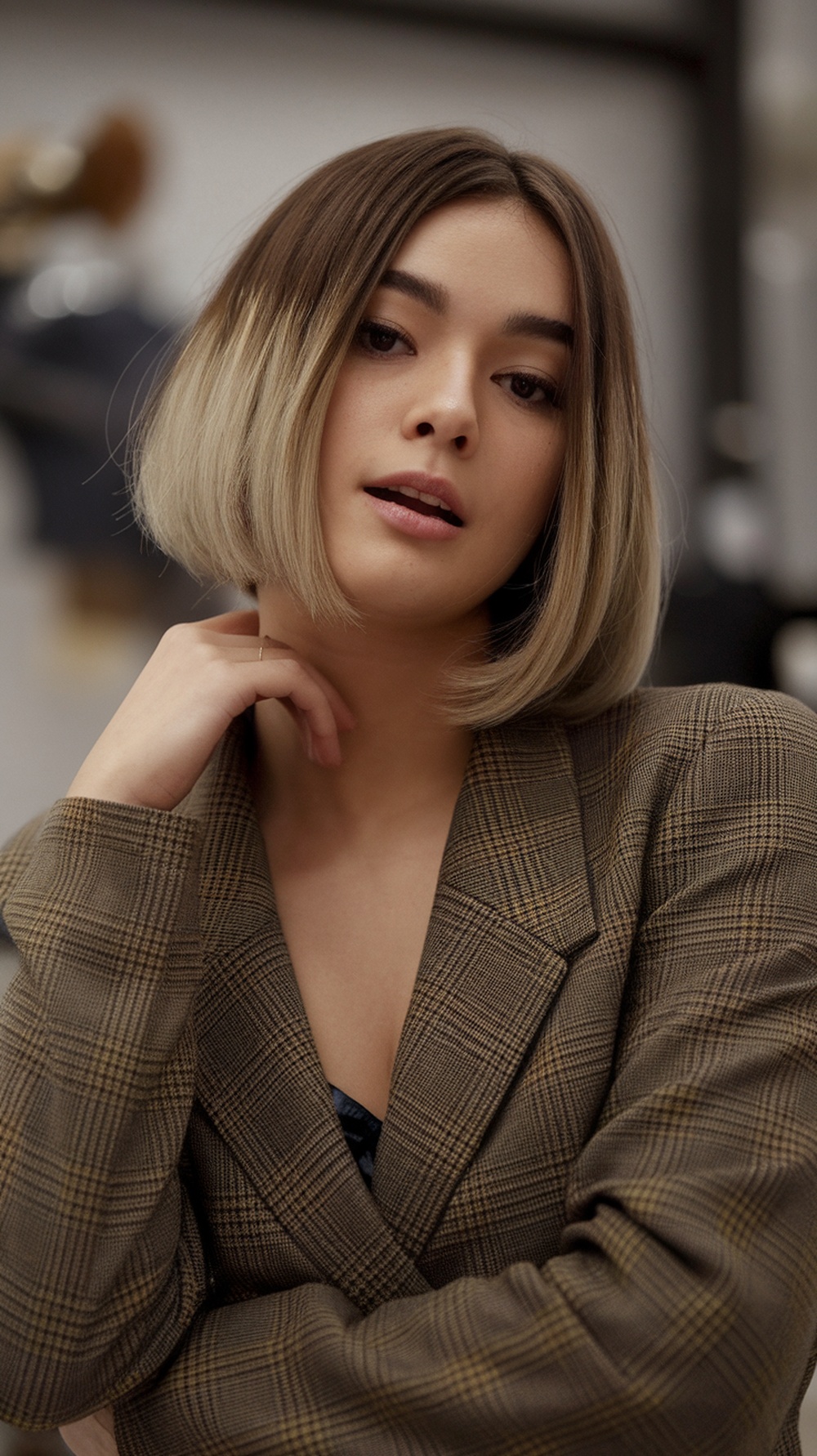 A woman with an asymmetrical bob hairstyle, featuring a shorter side and longer side, wearing a stylish blazer.
