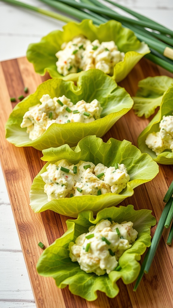 Lettuce wraps filled with egg salad, garnished with chives on a wooden board.